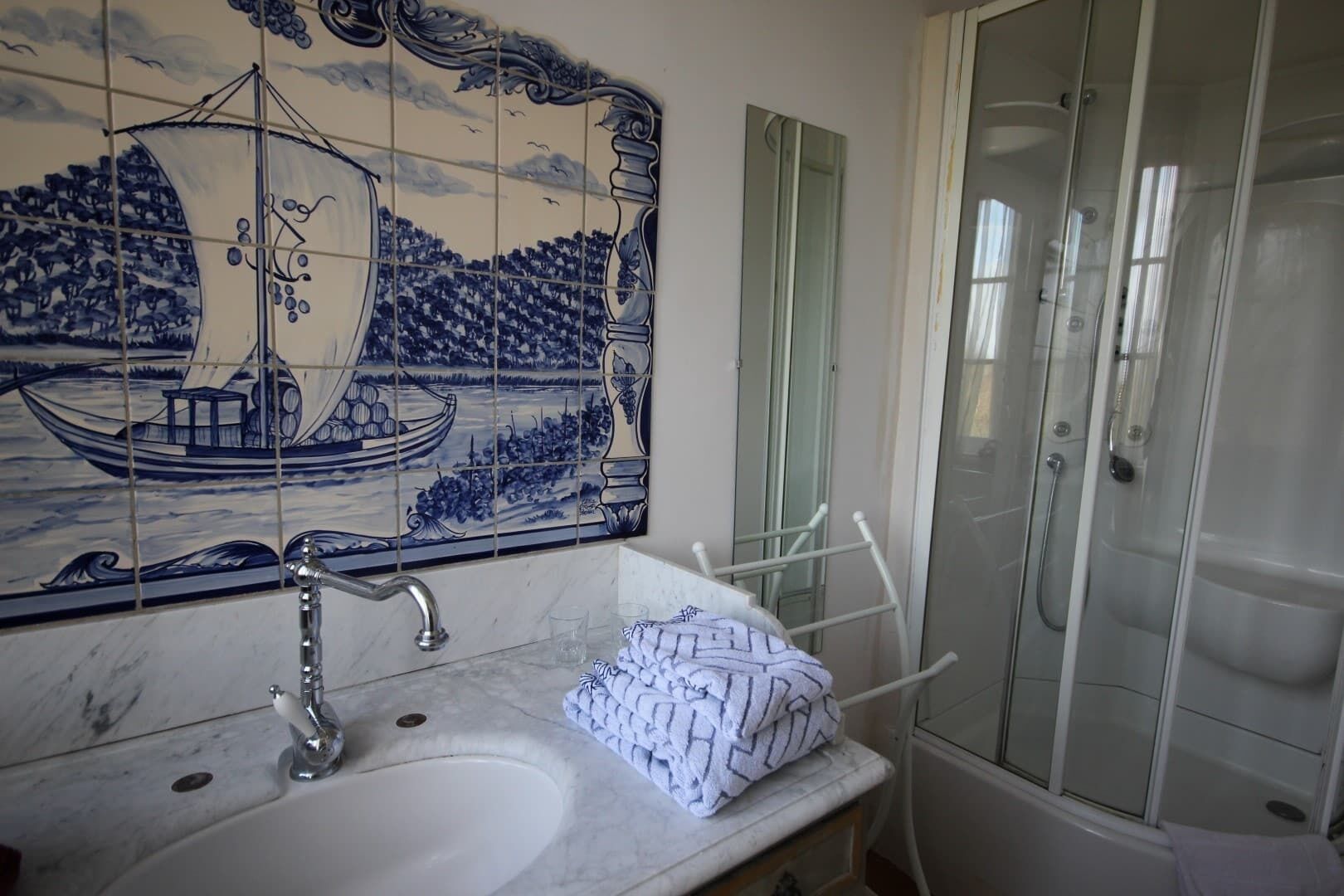 Un bany amb una paret revestida de rajoles, un lavabo, un mirall i una cabina de dutxa.