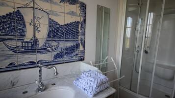 Un bany amb una paret revestida de rajoles, un lavabo, un mirall i una cabina de dutxa.
