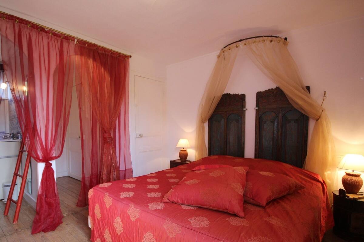 Un dormitorio con una cama grande, un cabecero de madera, una mesita de noche con lámpara y una ventana con cortinas.