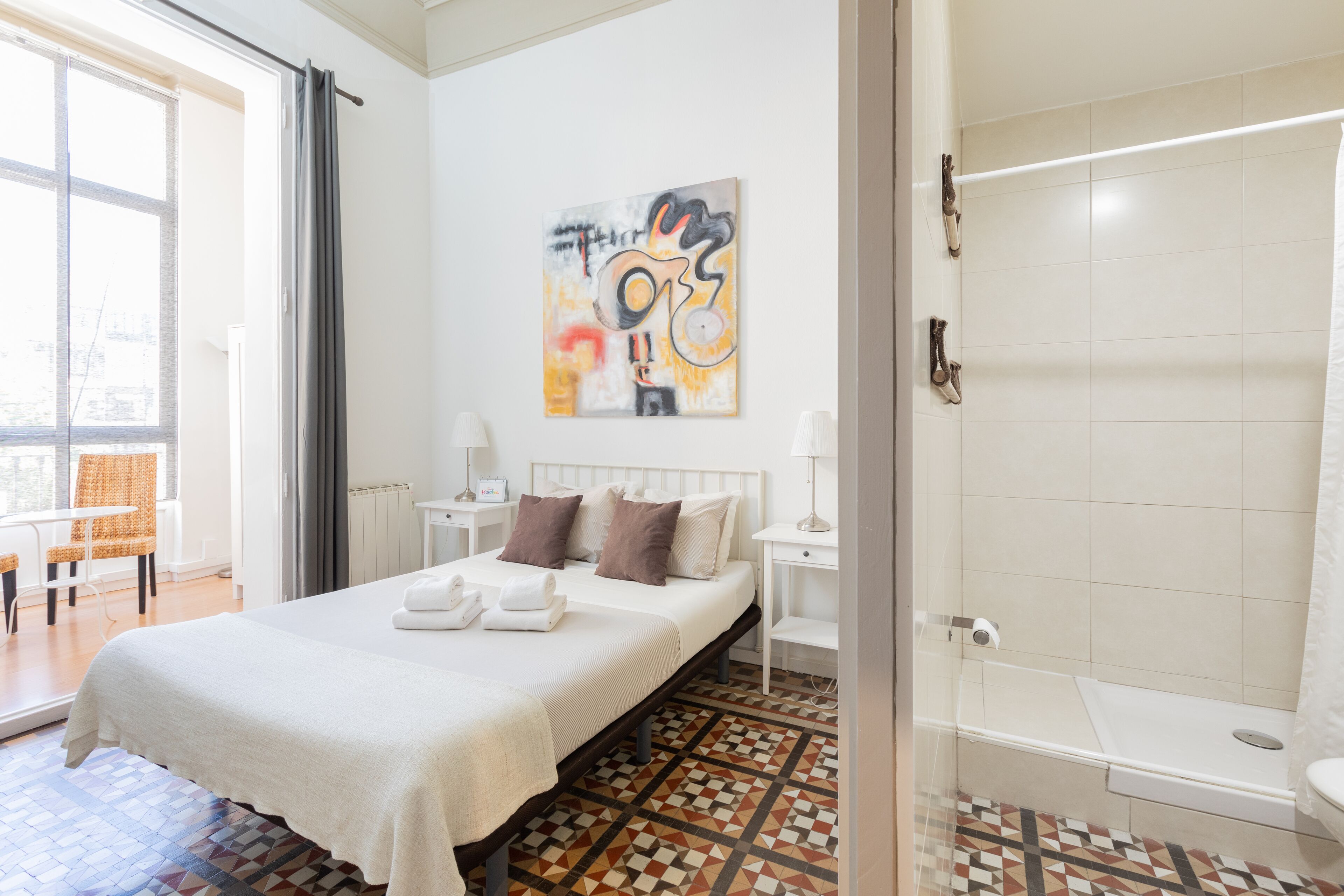 A hotel room with a bed, a shower, a window, and a painting on the wall.
