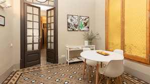 A room with a patterned floor, a round table with chairs, a bookshelf, and two framed pictures on the wall. - CasaNova Guest House (Barcelona)