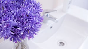 A clear view of a bathroom sink with a white faucet and a clear vase with purple flowers. - CasaNova Guest House (Barcelona)