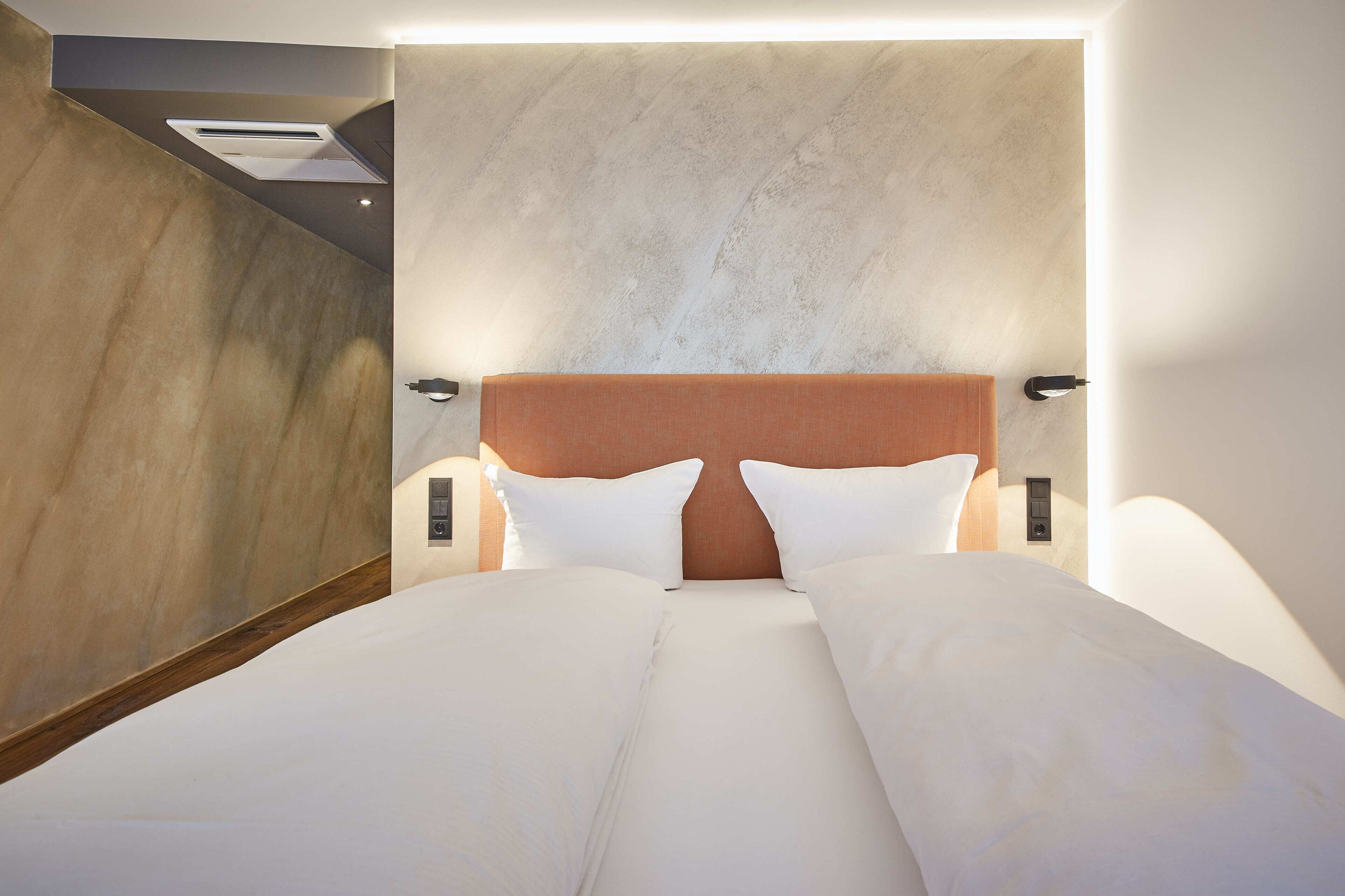 Quarto de hotel moderno com uma cama grande, painel de parede em madeira e unidade de ar condicionado integrada.