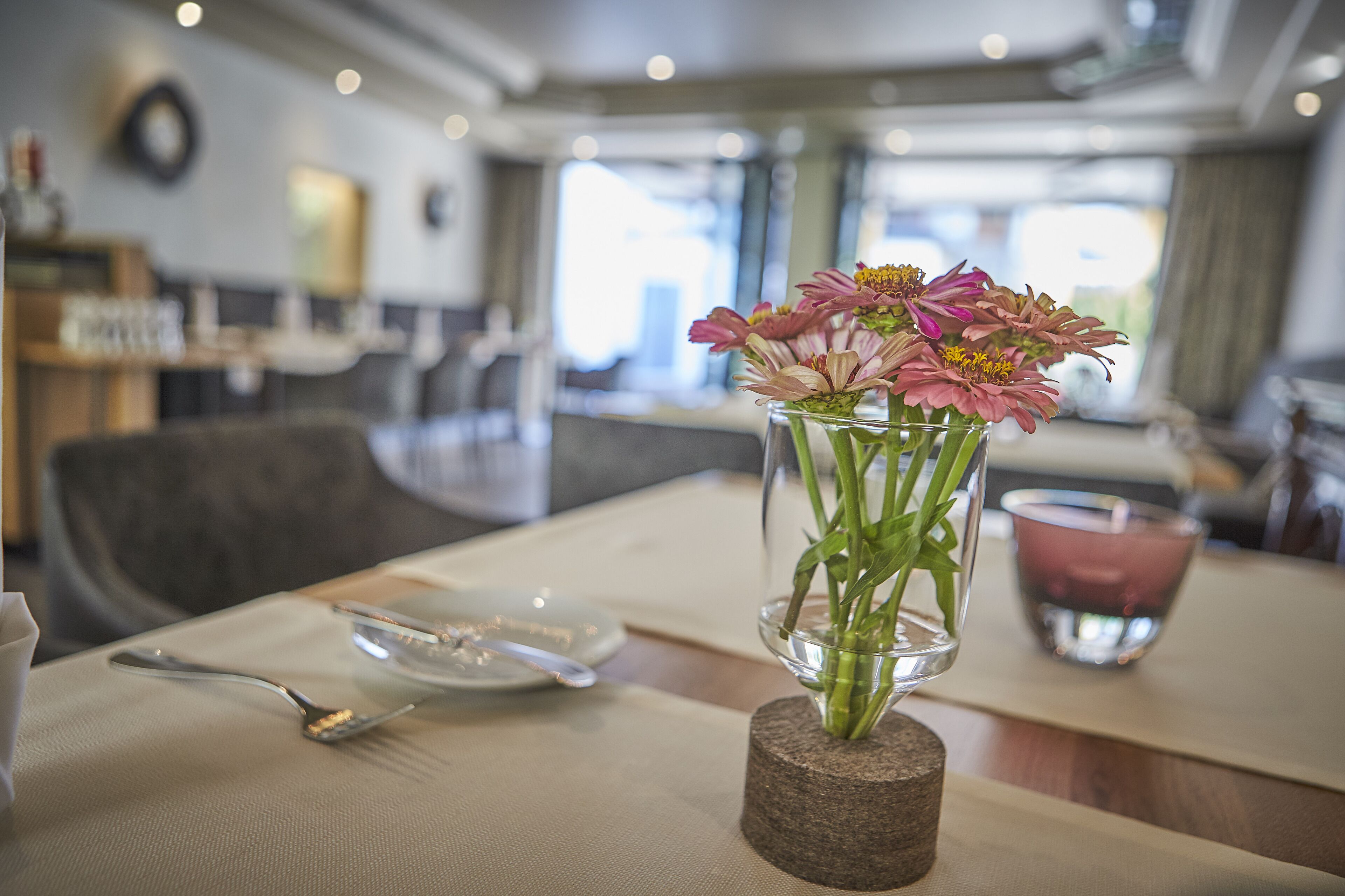 A dining table with a clear glass vase containing flowers, a spoon, and a plate.