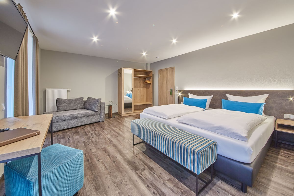 Quarto de hotel moderno com uma cama grande, um sofá, uma escrivaninha e um guarda-roupa.