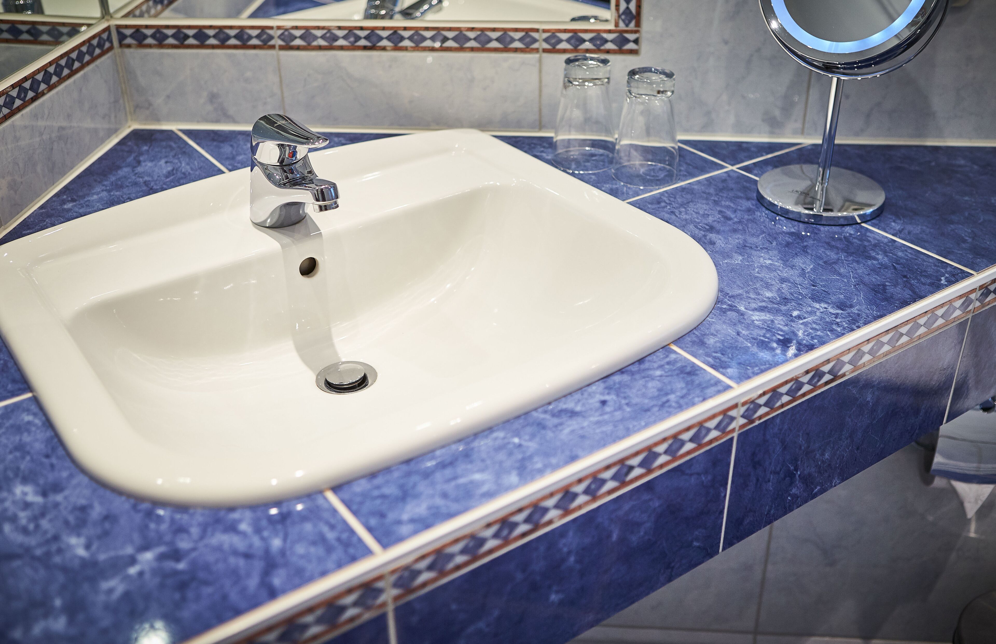 Un baño con lavamanos blanco, encimera de mármol azul y espejo con marco redondo.