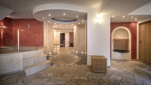Un intérieur spacieux avec un sol en pierre, un escalier central et une grande porte en arc de cercle.