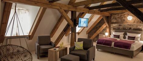 Un dormitorio tipo loft con vigas de madera a la vista, un sillón colgante, dos sillones, una cama con cabecera y un televisor en el techo.