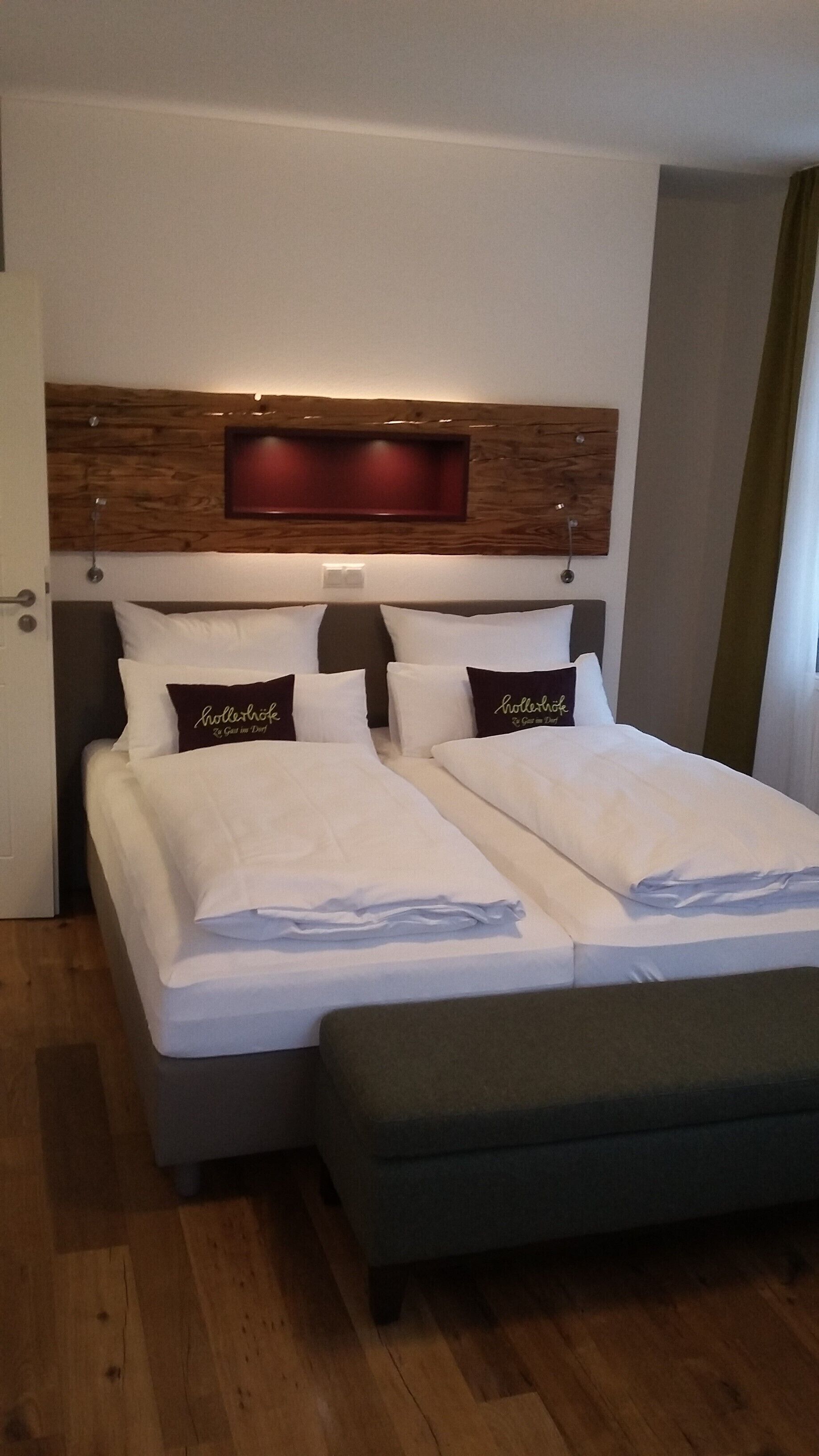 A double bed with white linens and two pillows with text, a wooden headboard, and a bedside table.