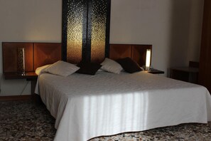 A neatly made bed with a white bedspread and two pillows, flanked by nightstands with lamps. - Domus Orsoni (Venice)