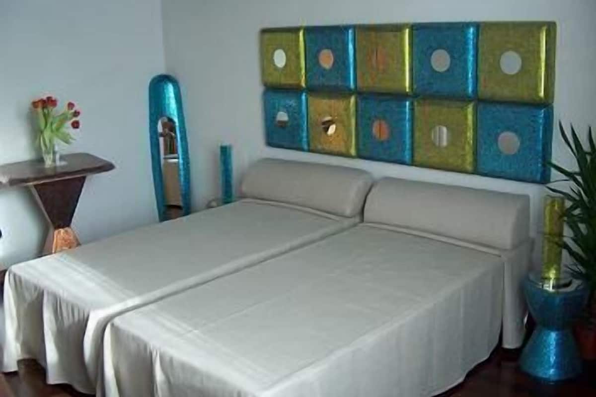Una habitación con una cama, una mesita con un florero y un panel decorativo en la pared.