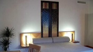 A hotel room with a bed, bedside lamps, a chair, a small table, and a decorative screen. - Domus Orsoni (Venice)