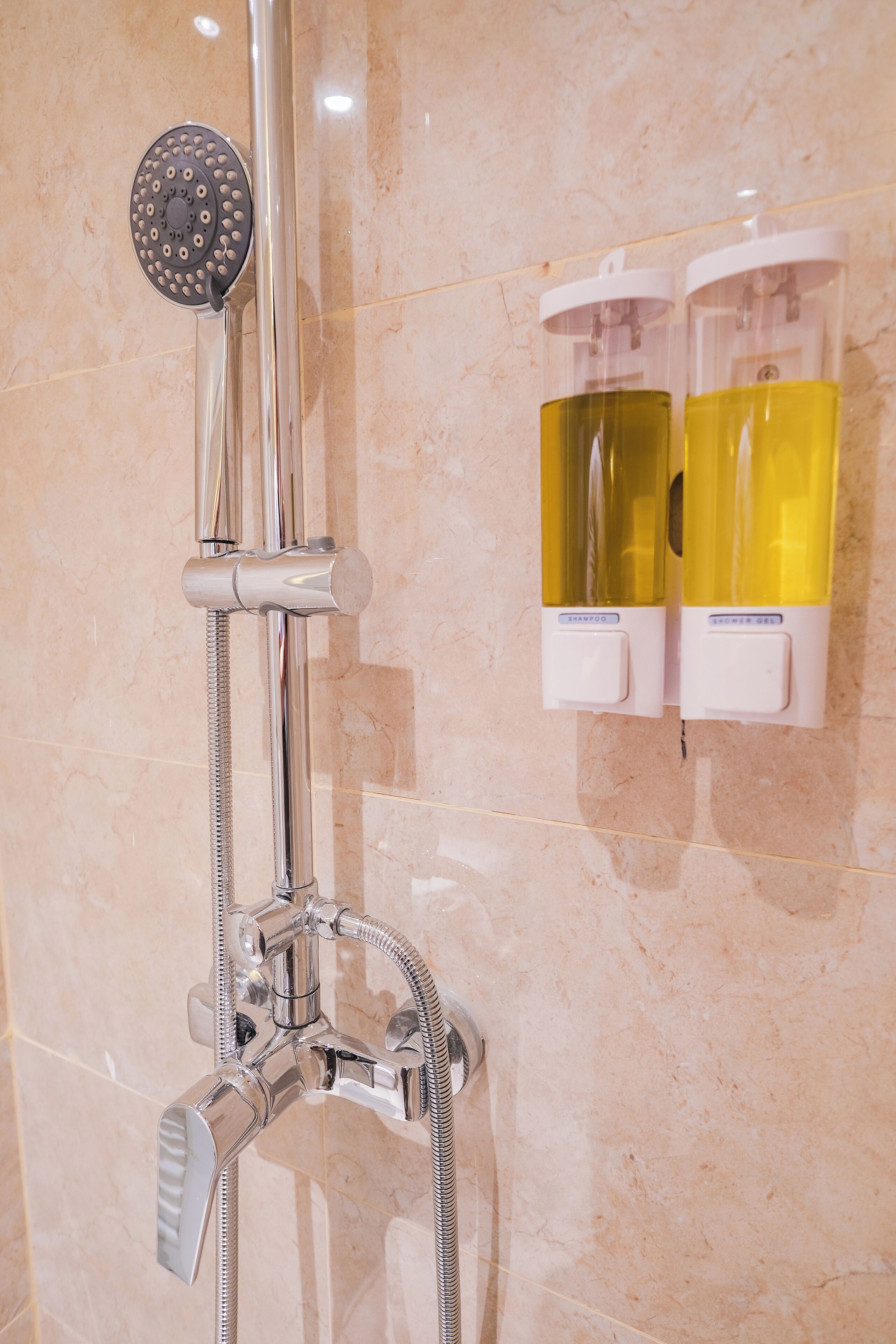 Chuveiro com chuveiro manual e torneira fixada na parede, e dois dispensadores de shampoo.