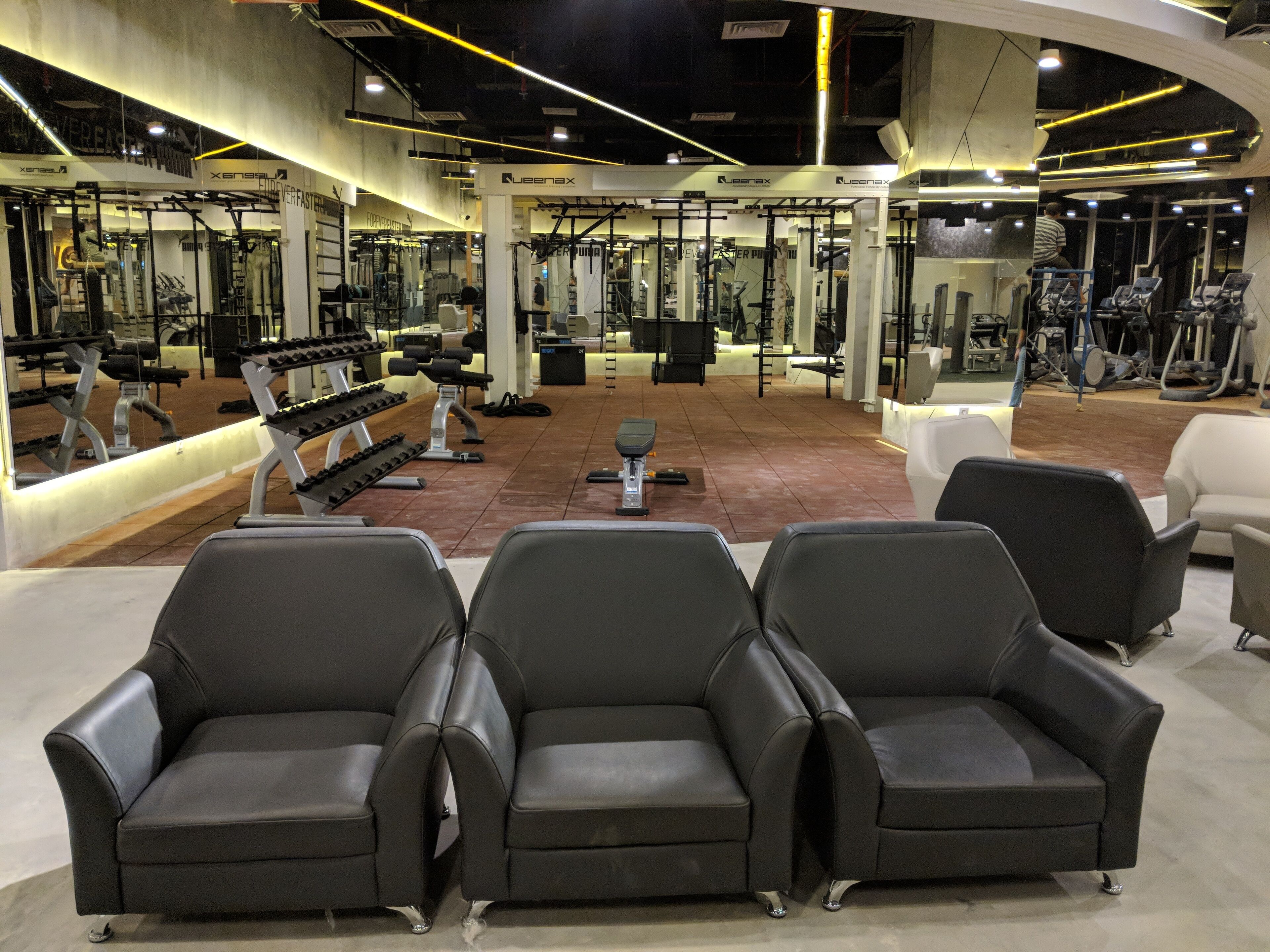 Een fitnessruimte met zwarte leren stoelen, trainingsapparatuur en spiegels.