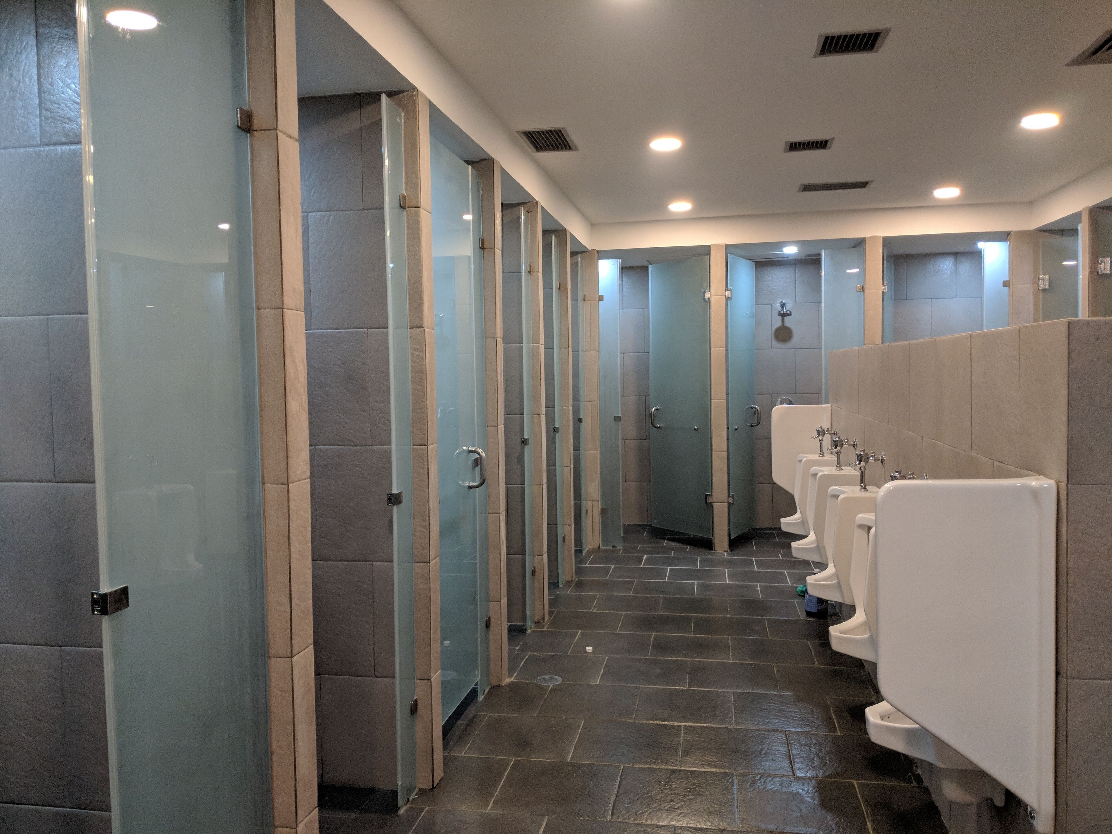 A row of public restrooms with glass partitions and white urinals.