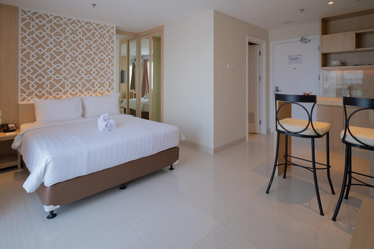 Een hotelkamer met een bed, een bureau en een stoel. Er is een deur naar een badkamer en een kitchenette.
