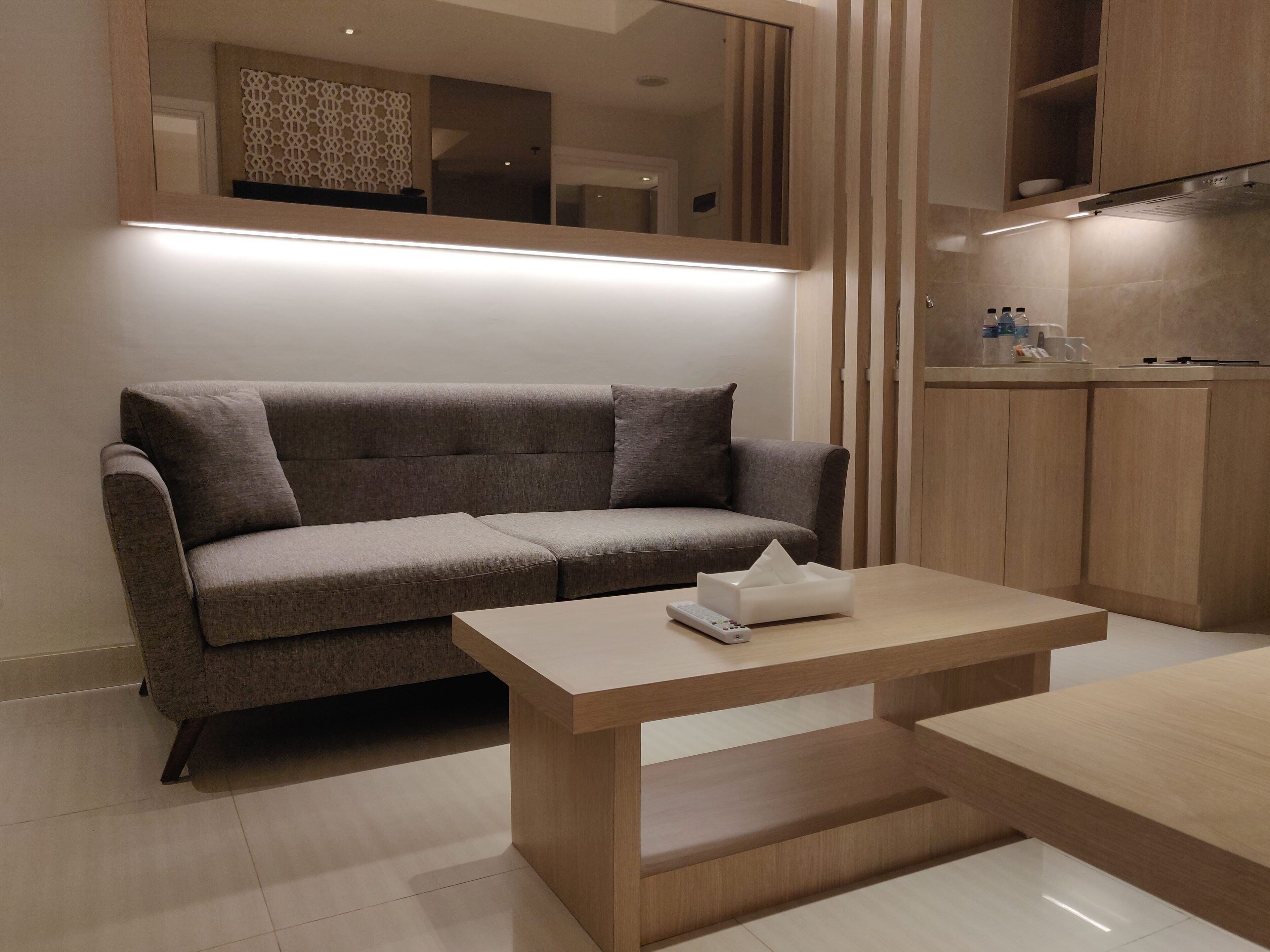 Un salon moderne avec un canapé gris, une table basse en bois et un coin cuisine doté de meubles et d’un plan de travail en bois.