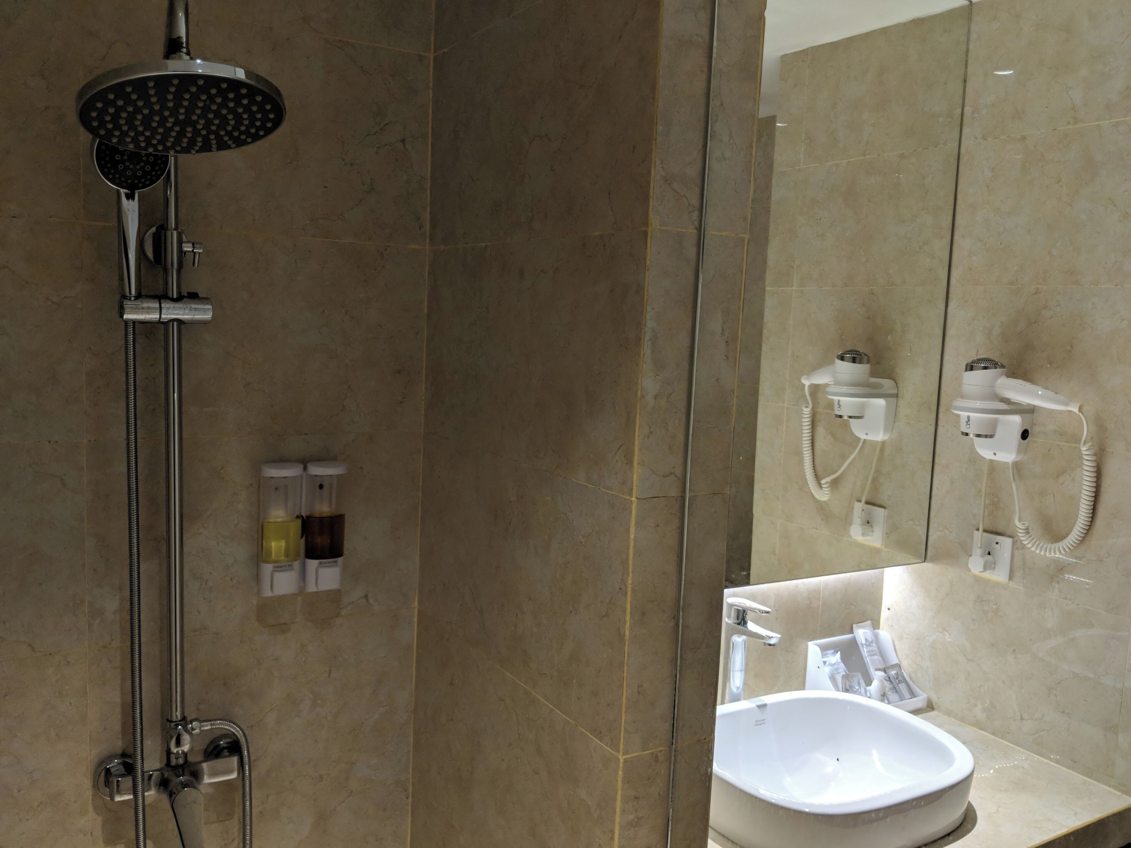 A bathroom with a shower, a sink, and a hairdryer mounted on the wall.