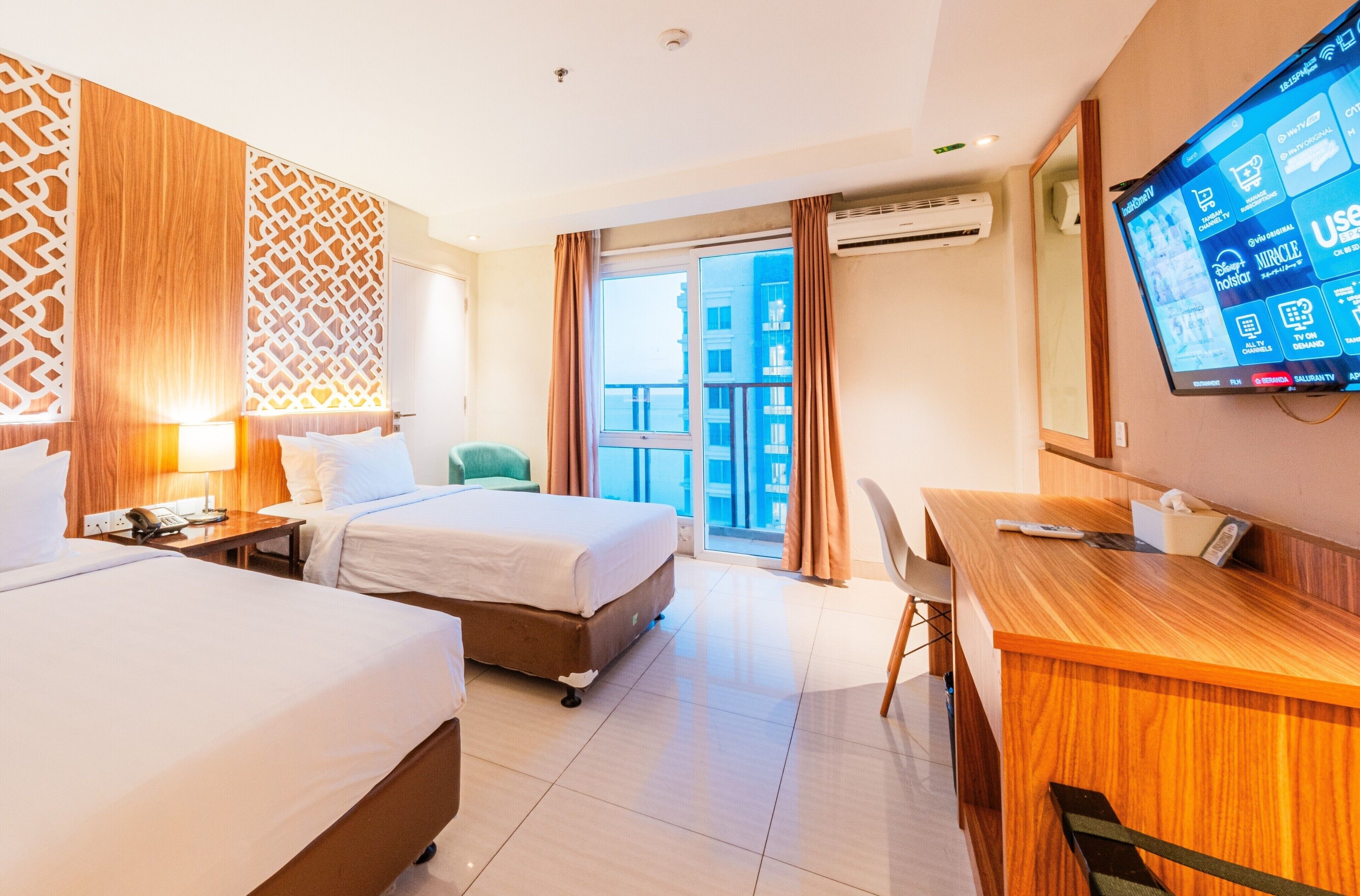 A hotel room with two beds, a desk, a TV, and a balcony with a view.