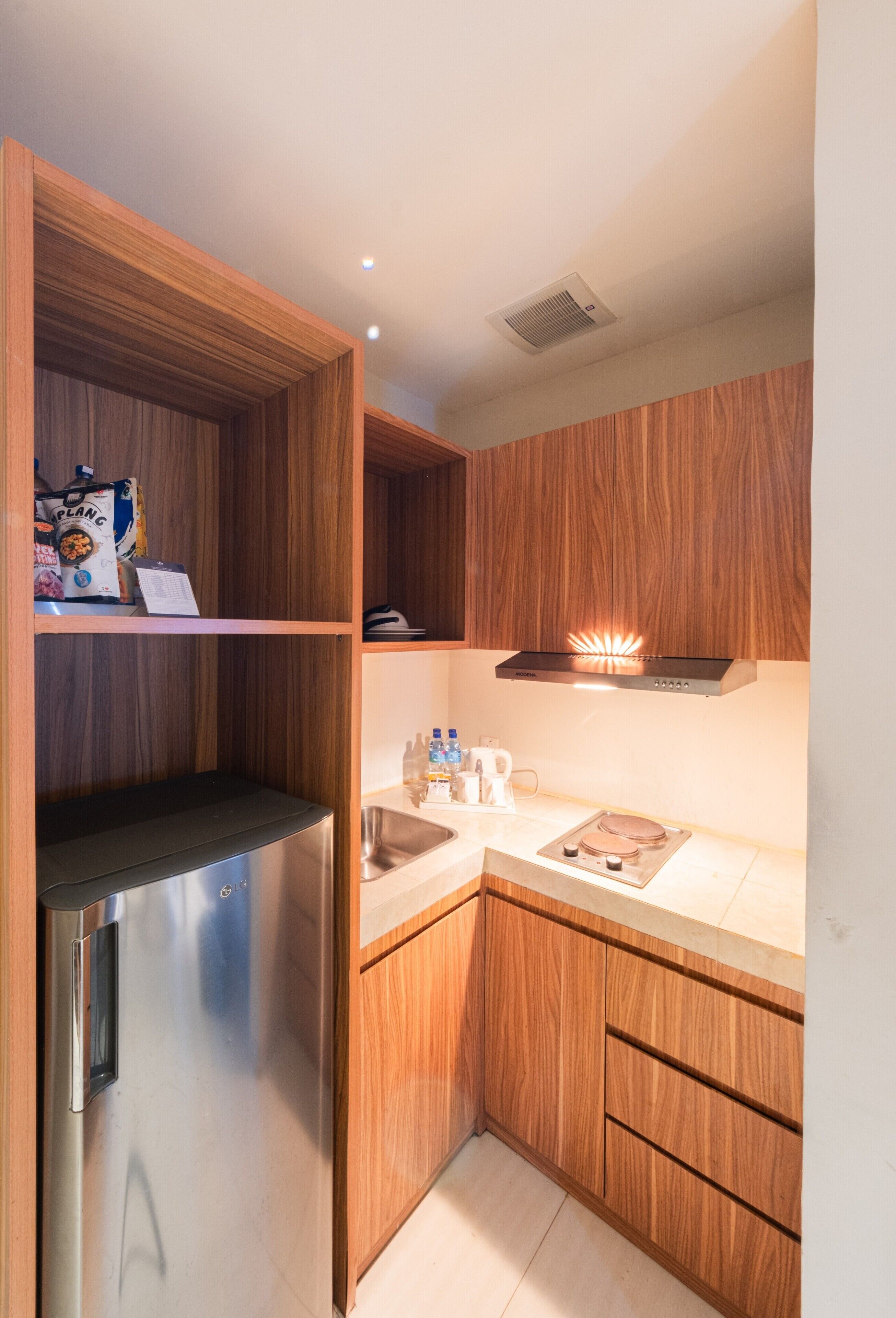 A compact kitchen with wooden cabinets, a stainless steel refrigerator, a built-in oven, and a microwave.