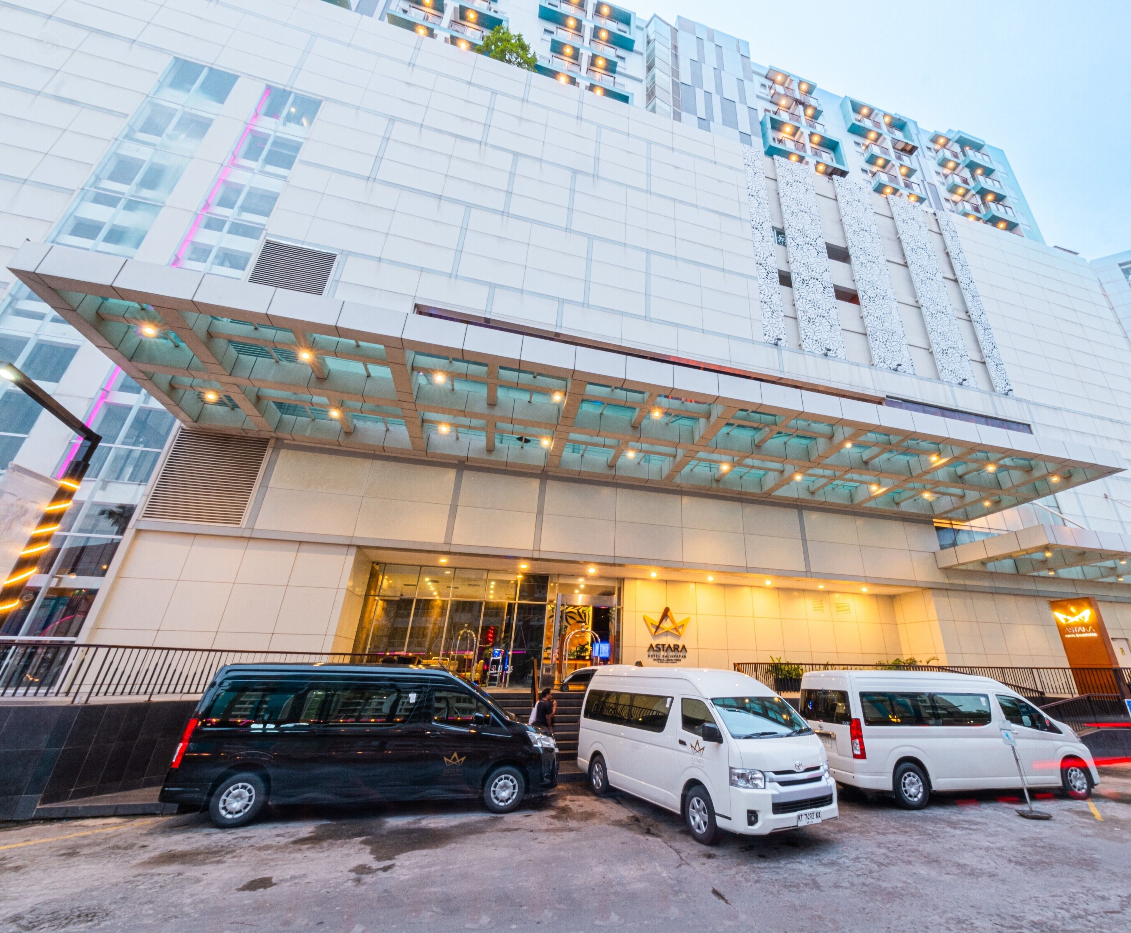 A modern building with a glass facade and a covered entrance. There are three vehicles parked in front.