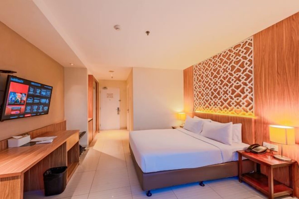 Een hotelkamer met een bed, nachtkastje, televisie en een decoratief paneel aan de muur.