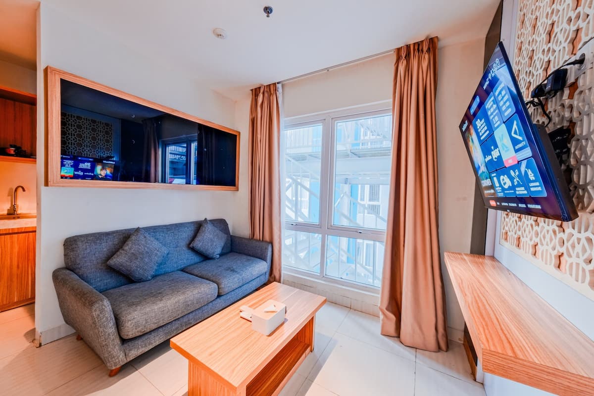 Een moderne woonkamer met een grijze bank, een houten salontafel en een aan de muur bevestigde televisie.