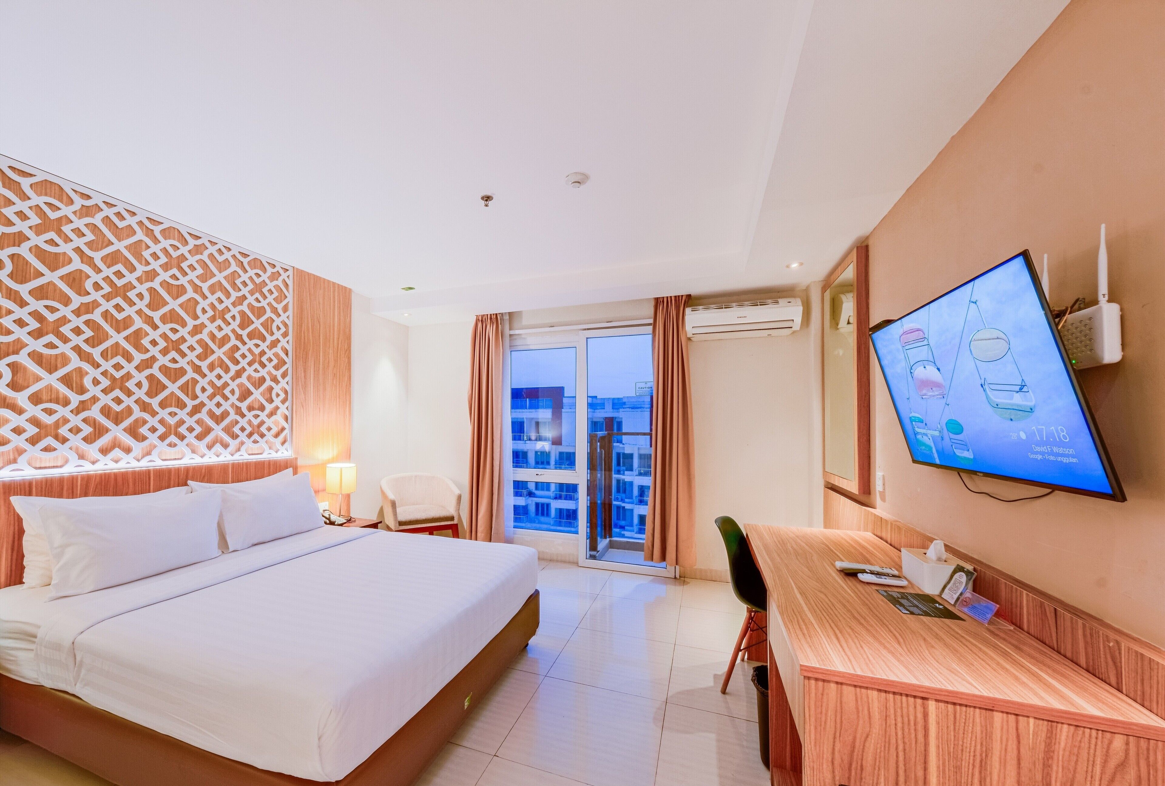 A hotel room with a bed, a desk, a television, and a view of the city through the window.