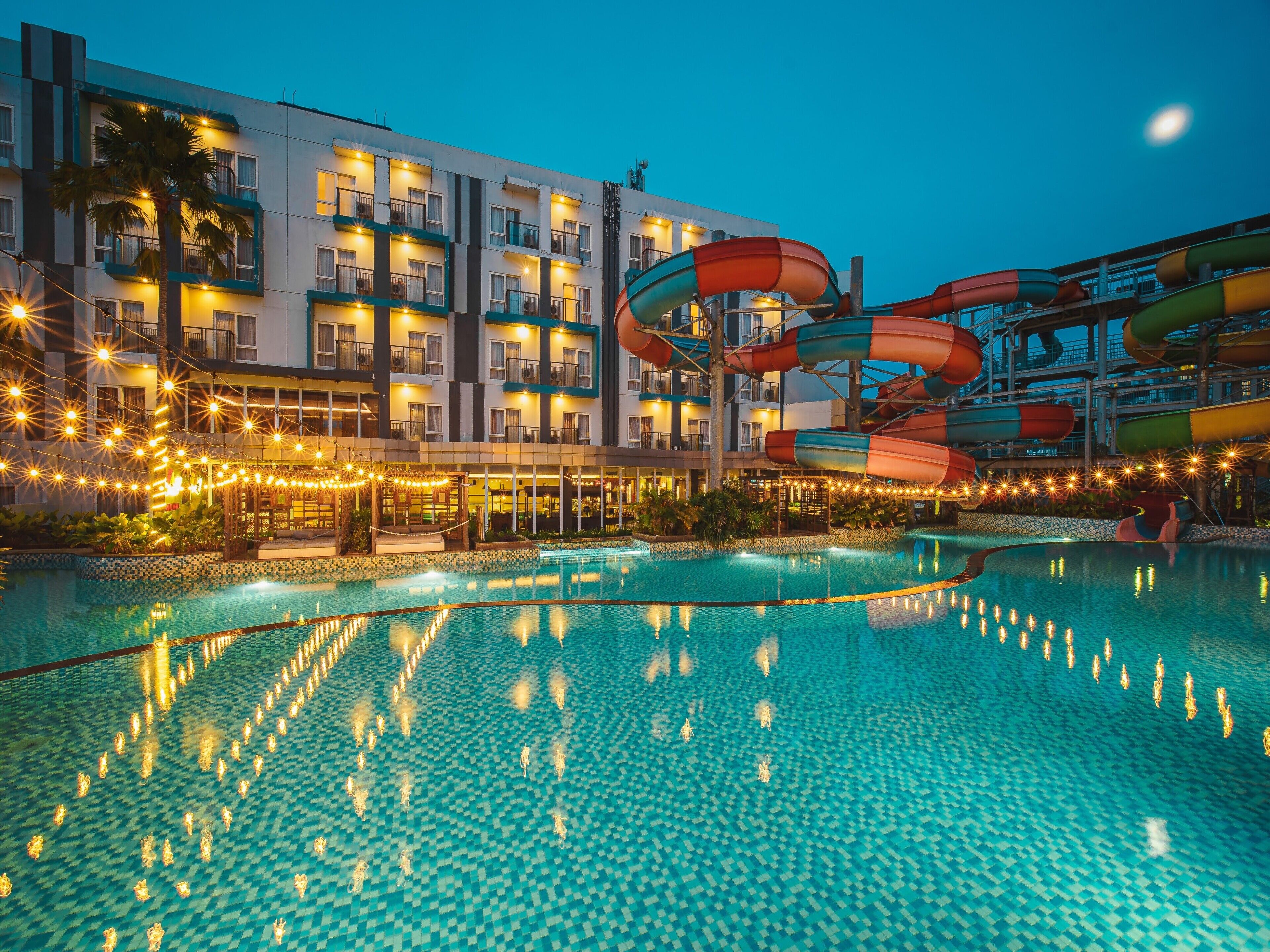 A hotel pool with a water slide and string lights.