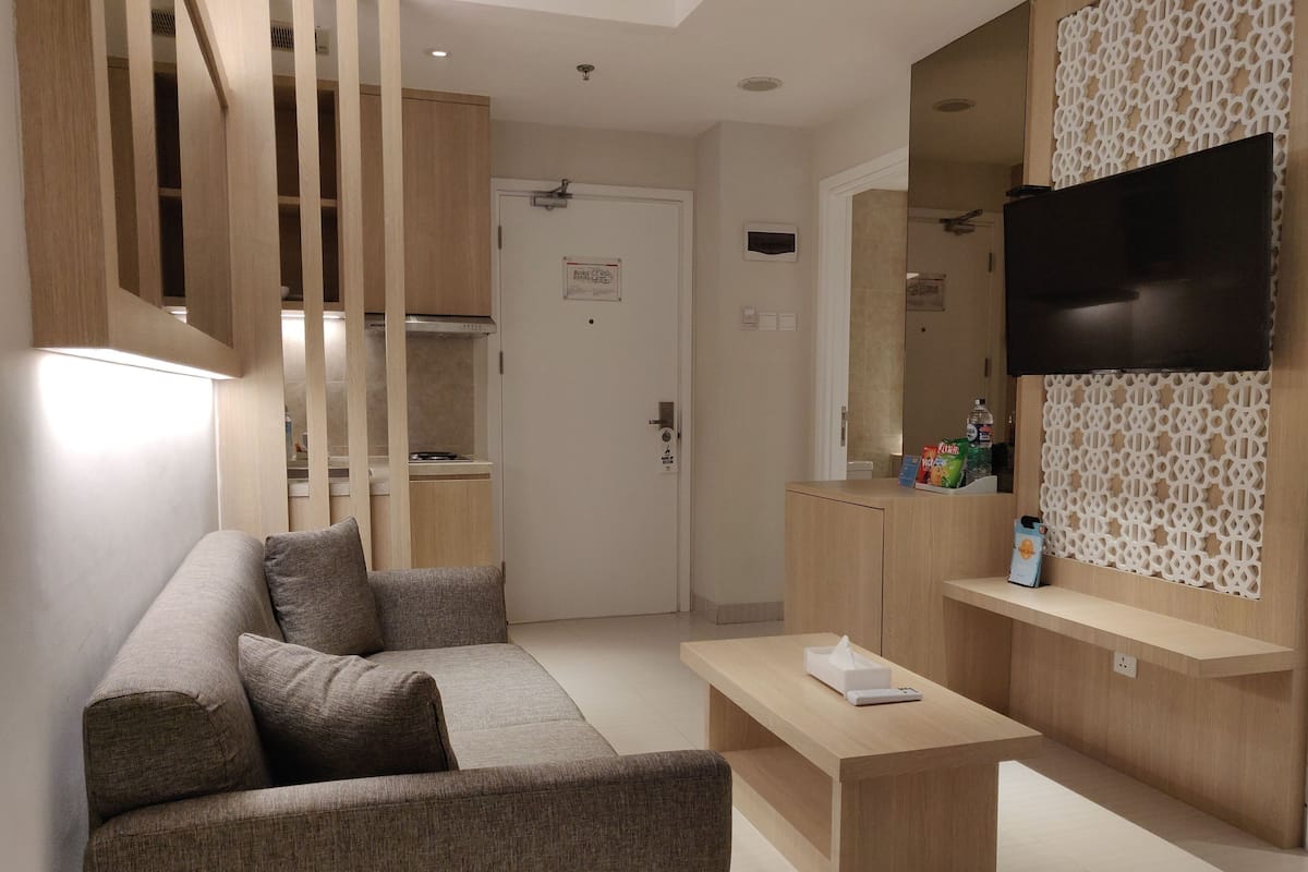Een moderne woonkamer met een bank, salontafel en een aan een wand met decoratieve panelen bevestigde televisie.