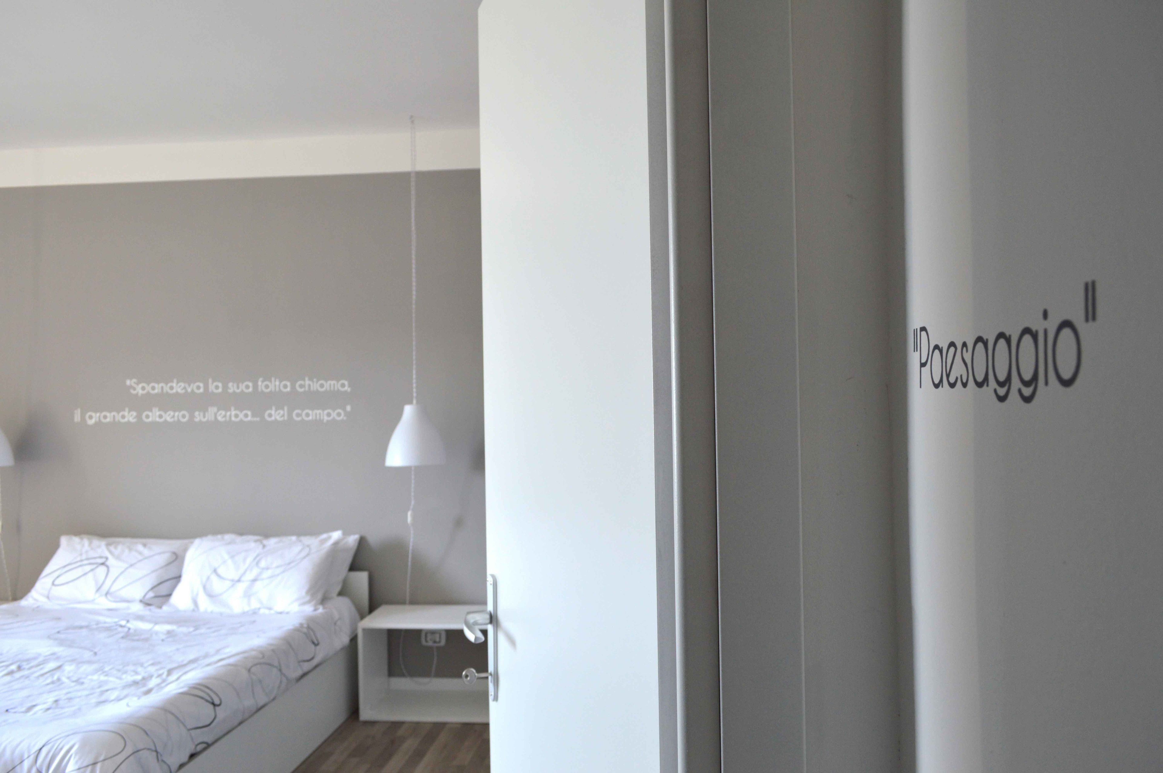 A minimalist bedroom with a bed, bedside table, and a wall with a quote.