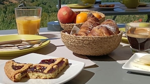 Una mesa servida con alimentos para el desayuno, como pasteles, frutas y bebidas, con vistas a un paisaje pintoresco.