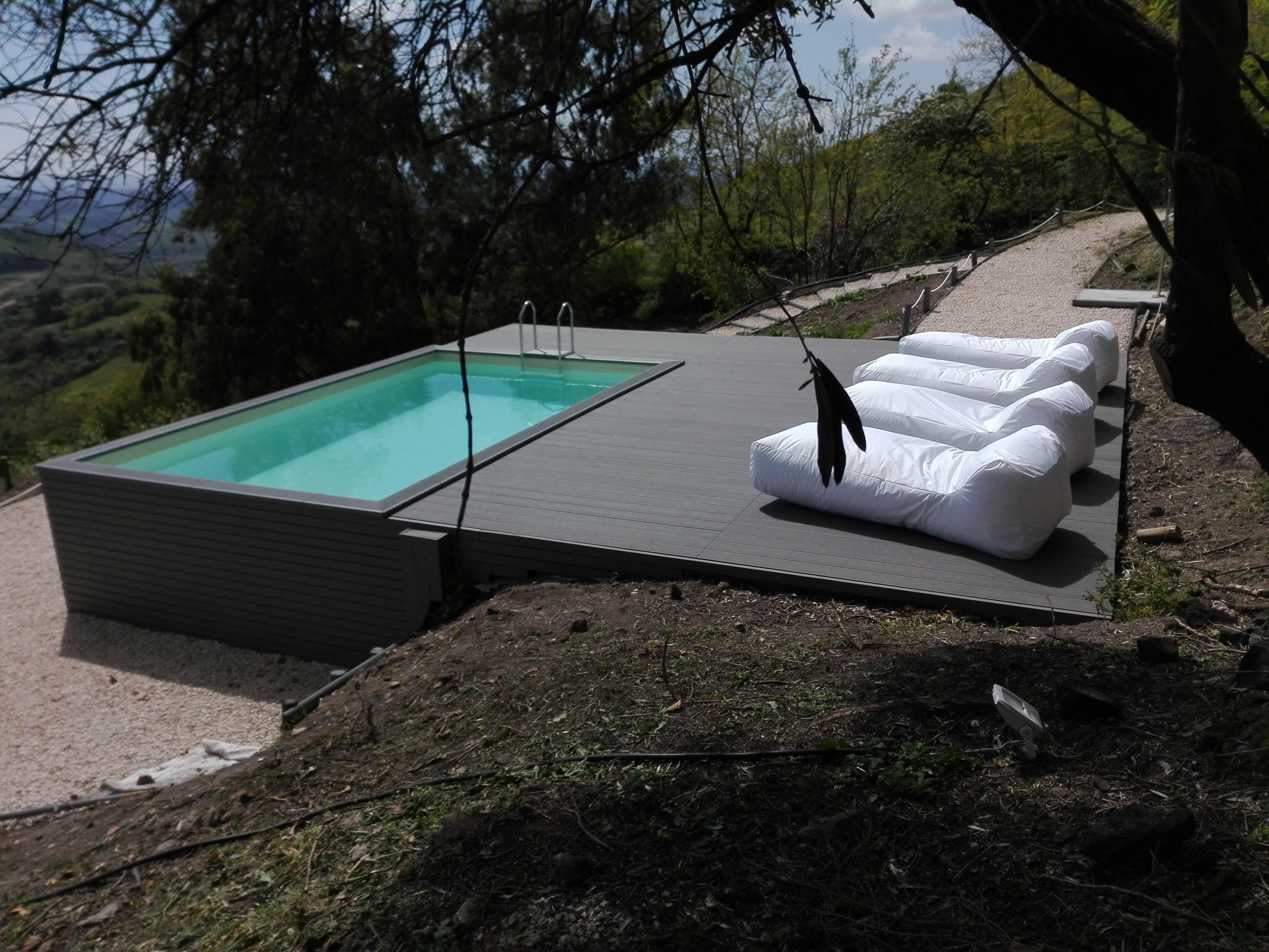 Une piscine extérieure moderne, dotée d’une terrasse, entourée de chaises longues et offrant une vue panoramique sur les collines.