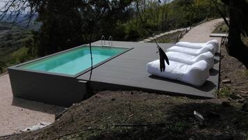 Une piscine extérieure moderne, dotée d’une terrasse, entourée de chaises longues et offrant une vue panoramique sur les collines.