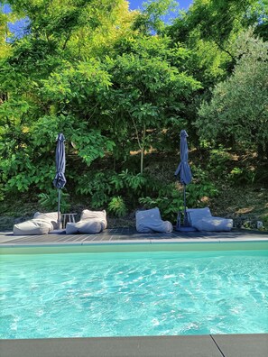 A pool area with lounge chairs and umbrellas, surrounded by lush greenery. - Tuffudesu B&B (Osilo)