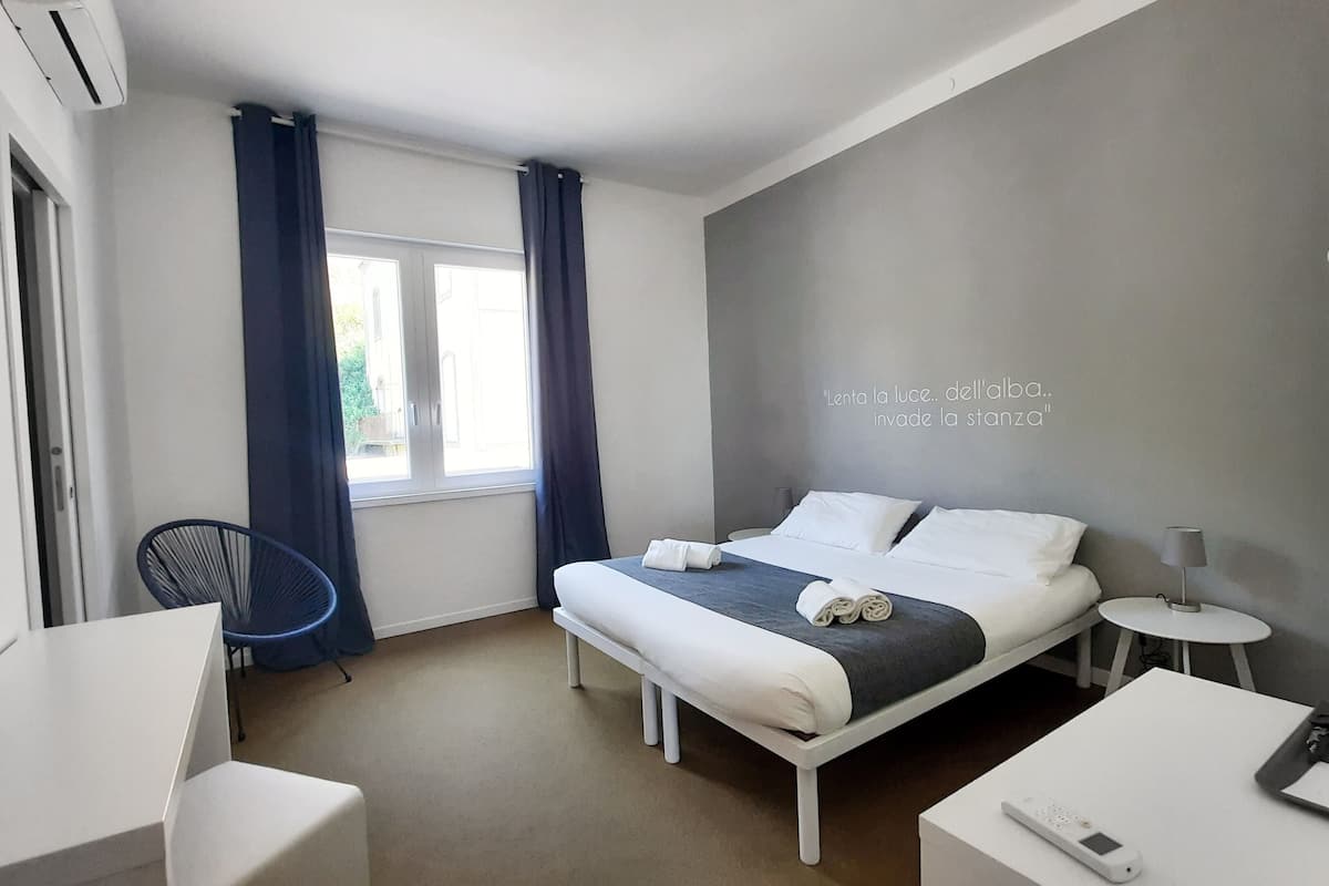 Una habitación de hotel moderna con una cama, mesitas de noche, una silla y un ventanal con cortinas.