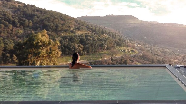 Una persona descansando en una piscina con vistas a un paisaje montañoso.