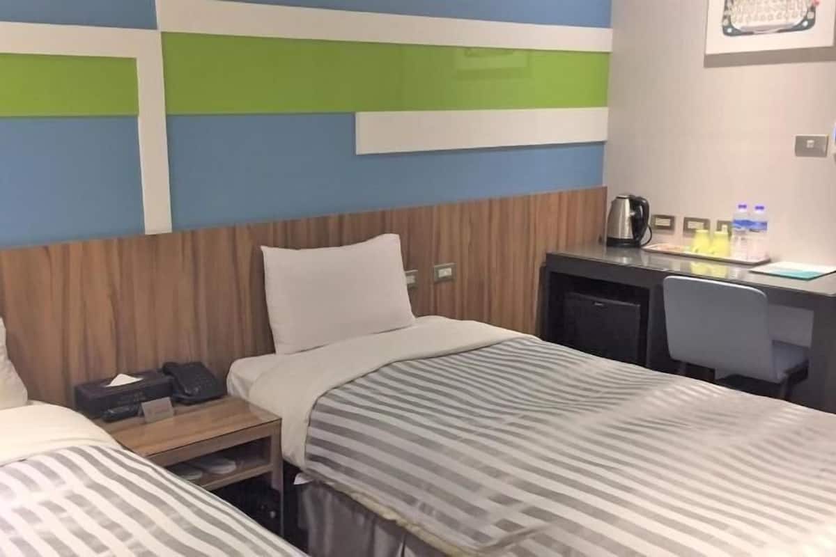 A hotel room with two beds, a desk, and a small kitchenette.