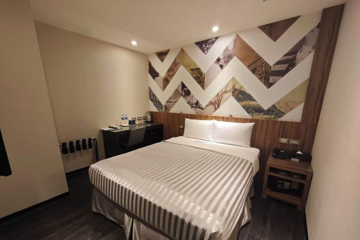 A hotel room with a bed, a desk, and a wall with geometric patterns.
