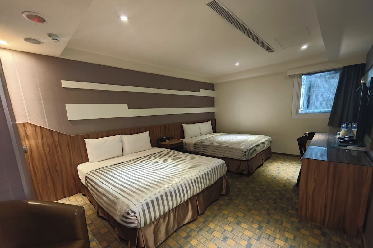 A hotel room with two beds, a desk, and a chair.