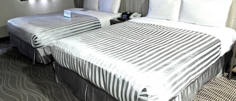 A hotel room with two beds, a patterned carpet, and a floral wallpaper.