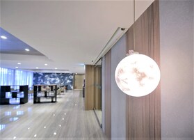 Un moderno vestíbulo de hotel con piso pulido, una recepción y una gran lámpara esférica fijada a la pared.