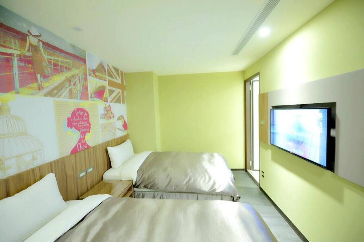 A hotel room with two beds, a large wall mural, and a television on the wall.