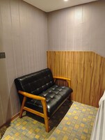 Un espacio pequeño y cerrado con un sofá de cuero negro, sillones de madera, alfombra estampada y papel tapiz texturizado.