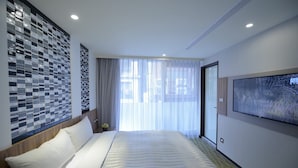 A modern hotel room with a large bed, a view through sheer curtains, a wall-mounted TV, and a patterned tile accent wall. - Ximen Hotel (Taipei)