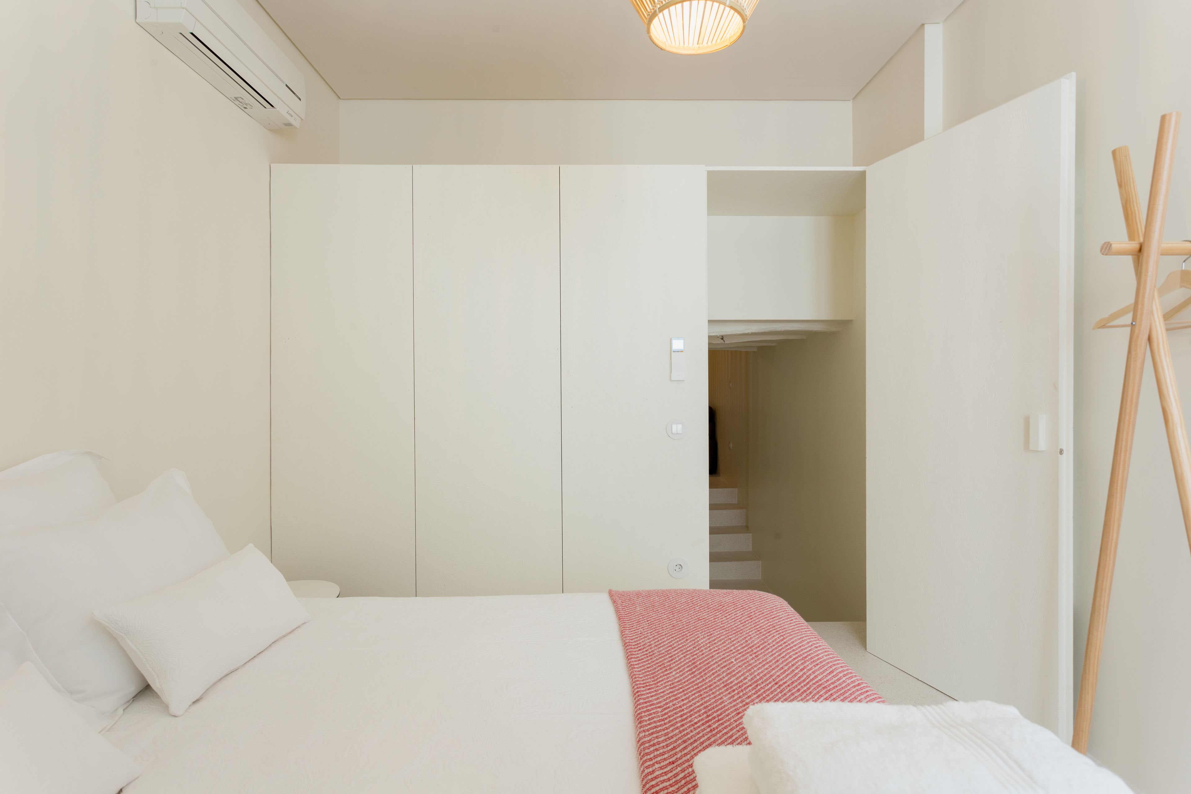A bedroom with a bed, white wardrobe, and a wooden coat rack.