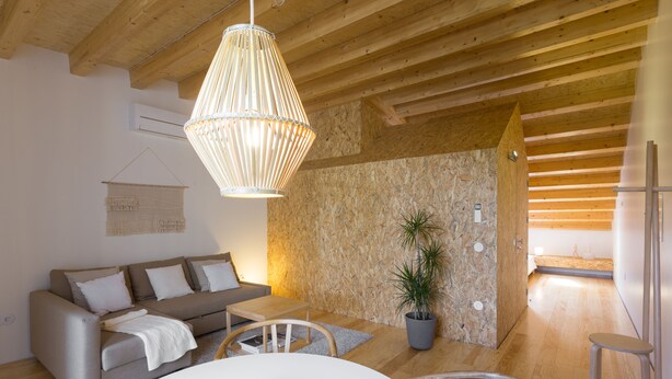 Una sala moderna con techo de madera, un sofá, una mesa de comedor y una lámpara colgante.