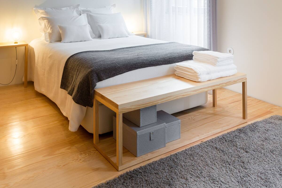 Quarto moderno com cama, mesa de cabeceira, luminária e aparelho de ar condicionado.