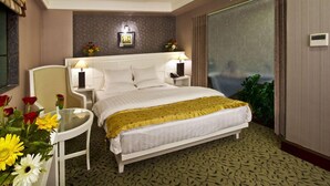 A hotel room with a bed, bedside tables, a chair, a small table with flowers, and a large mirror. - Gargee Grand Patna (Patna)