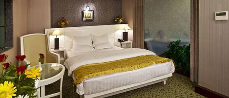 A hotel room with a bed, bedside tables, a chair, a small table with flowers, and a large mirror.